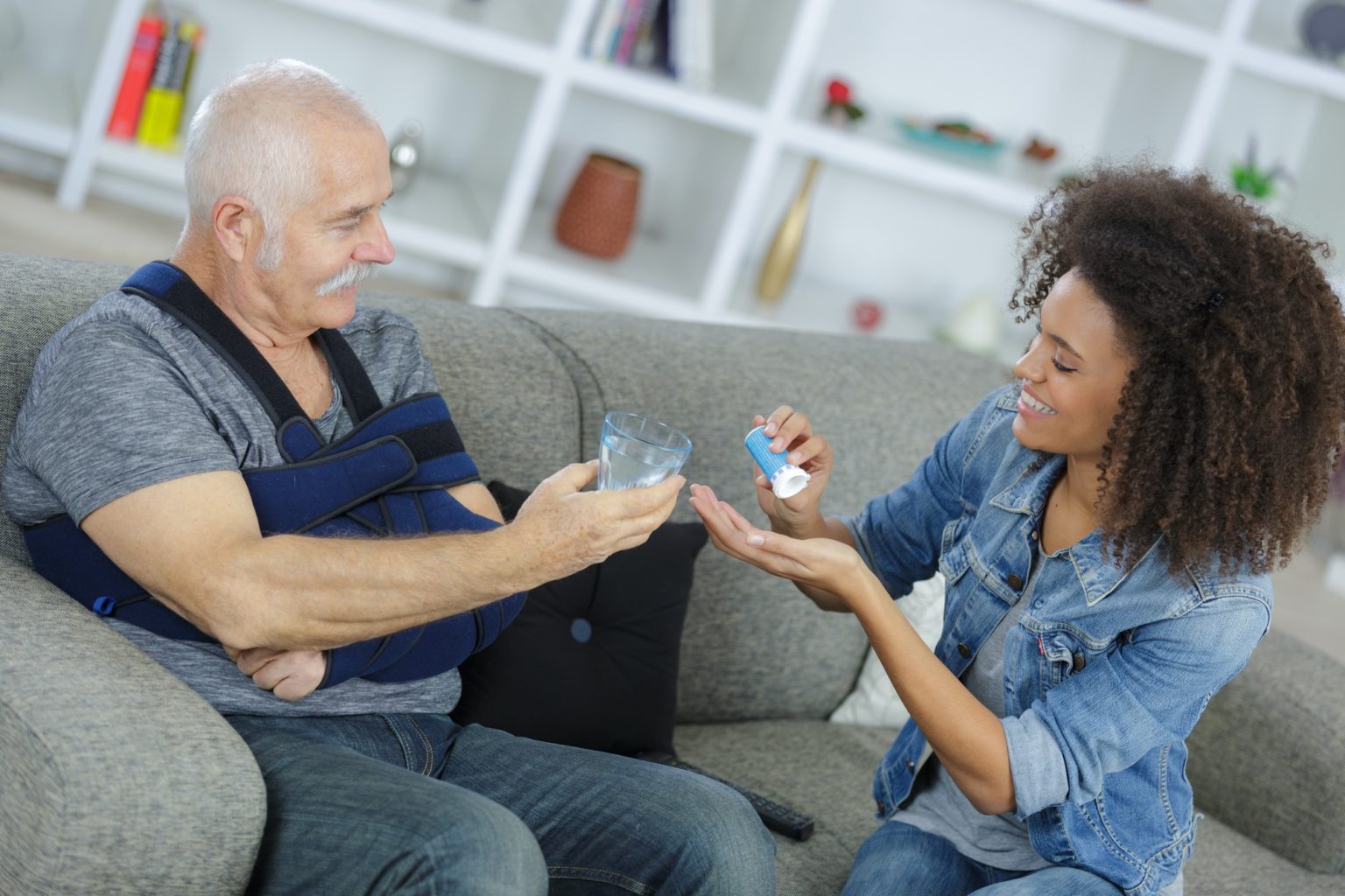 Lady preparing medication for senior man with his arm in a sling