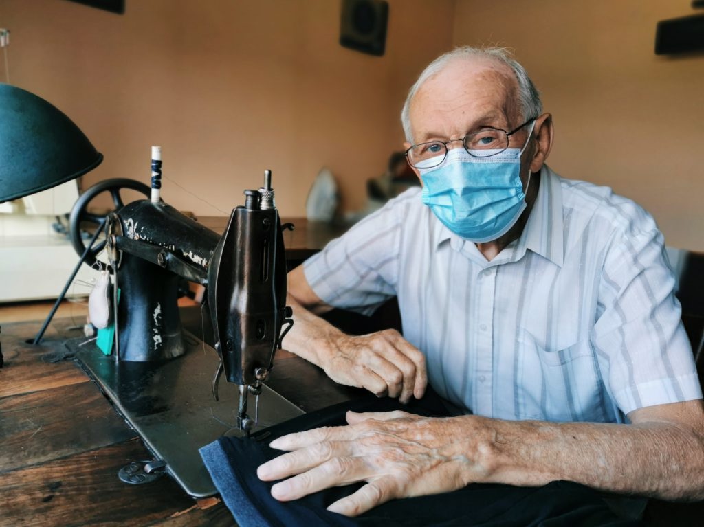 Old tailor wearing a protective surgical mask at home
