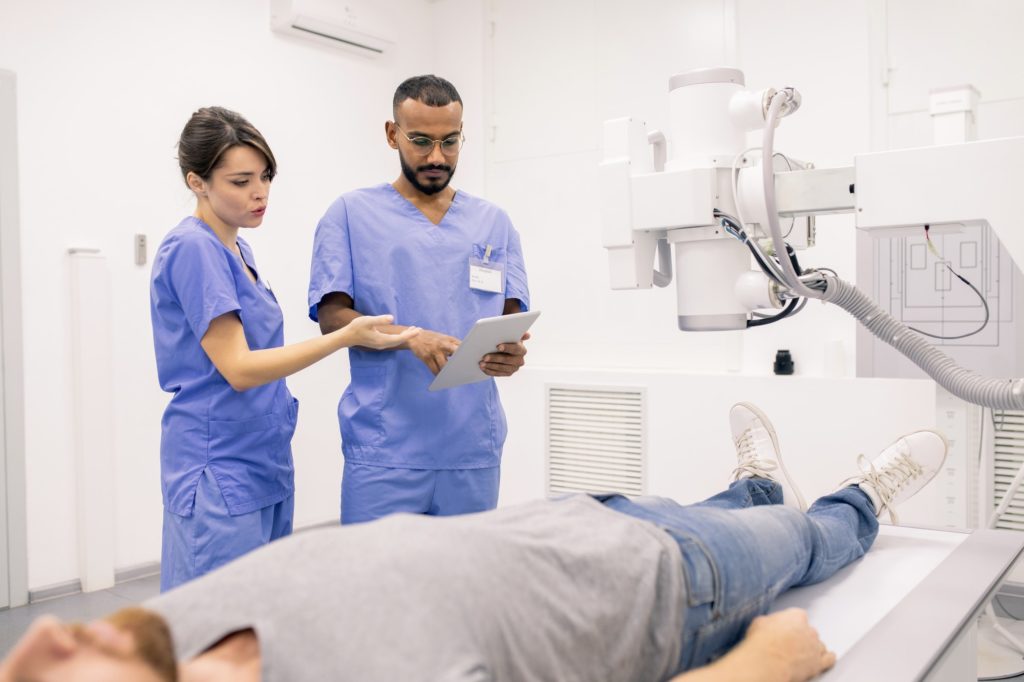 Two young clinicians in blue uniform discussing online data in touchpad