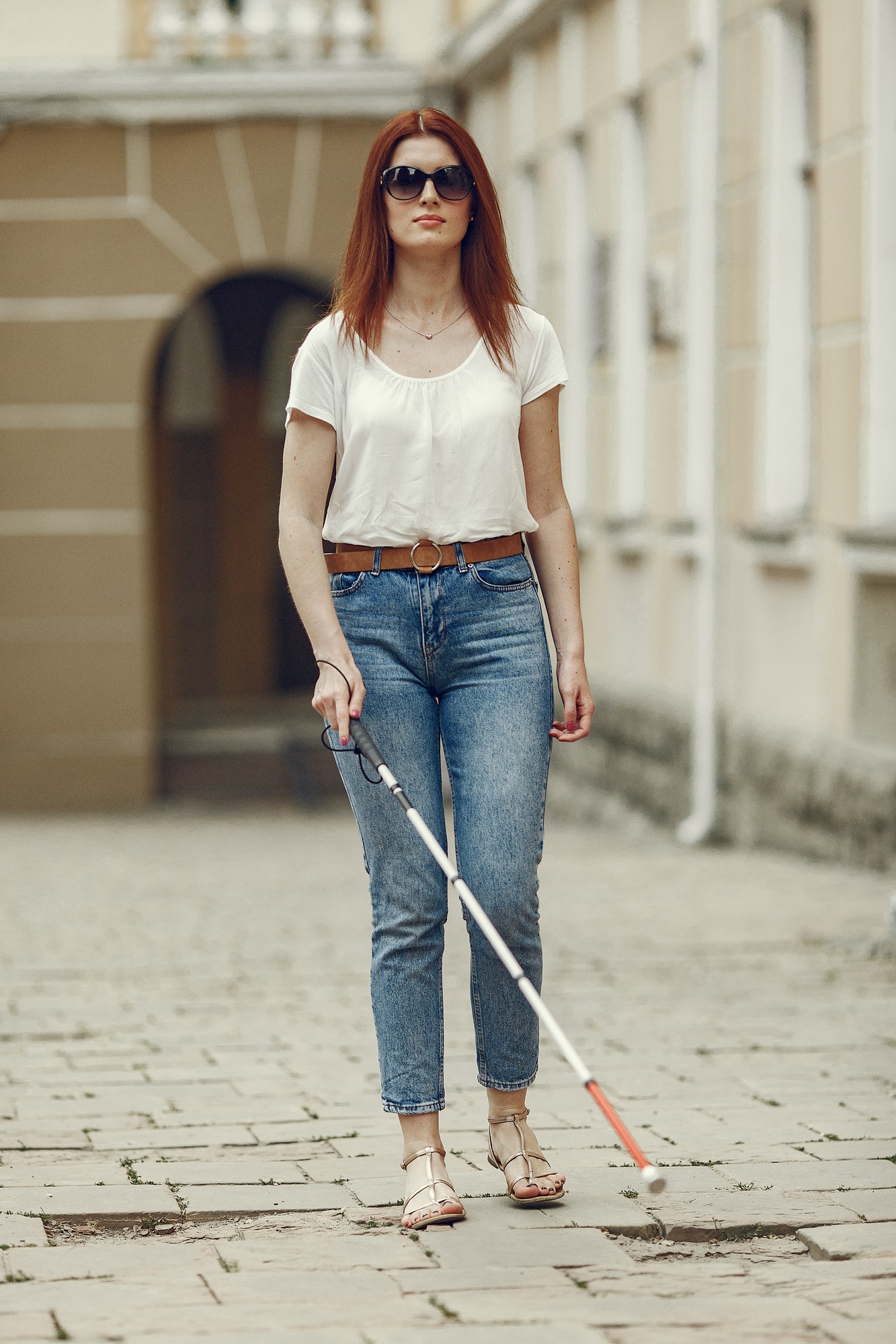 Young blind person with long cane walking in a city